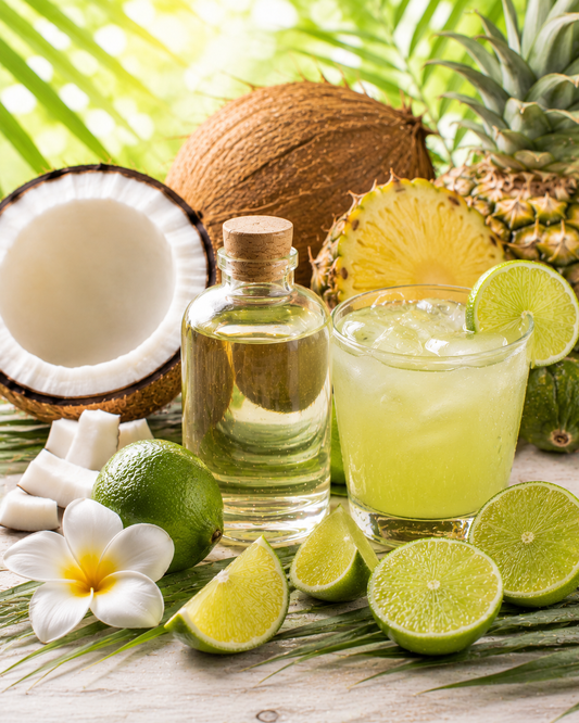 Glass of lime juice with a bottle of liquid, surrounded by coconuts, pineapple, limes, and flowers on a wooden surface.