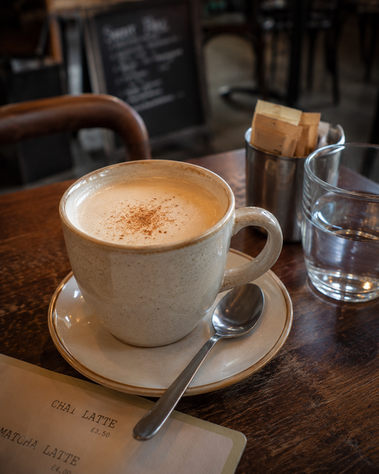 Chai latte in a white mug on a wooden table with a spoon and glass of water.