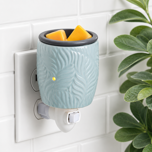 Wall-mounted teal wax warmer with two yellow wax melts on a tiled wall background.